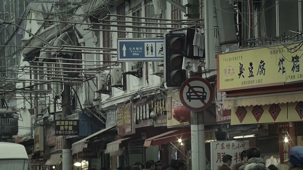 A busy street in an old city, with many signs and wires, and people walking below, under a grey sky.