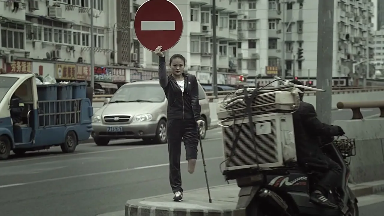 A young woman with a prosthetic leg holds up a stop sign on a busy city street, as a man on a scooter passes by.
