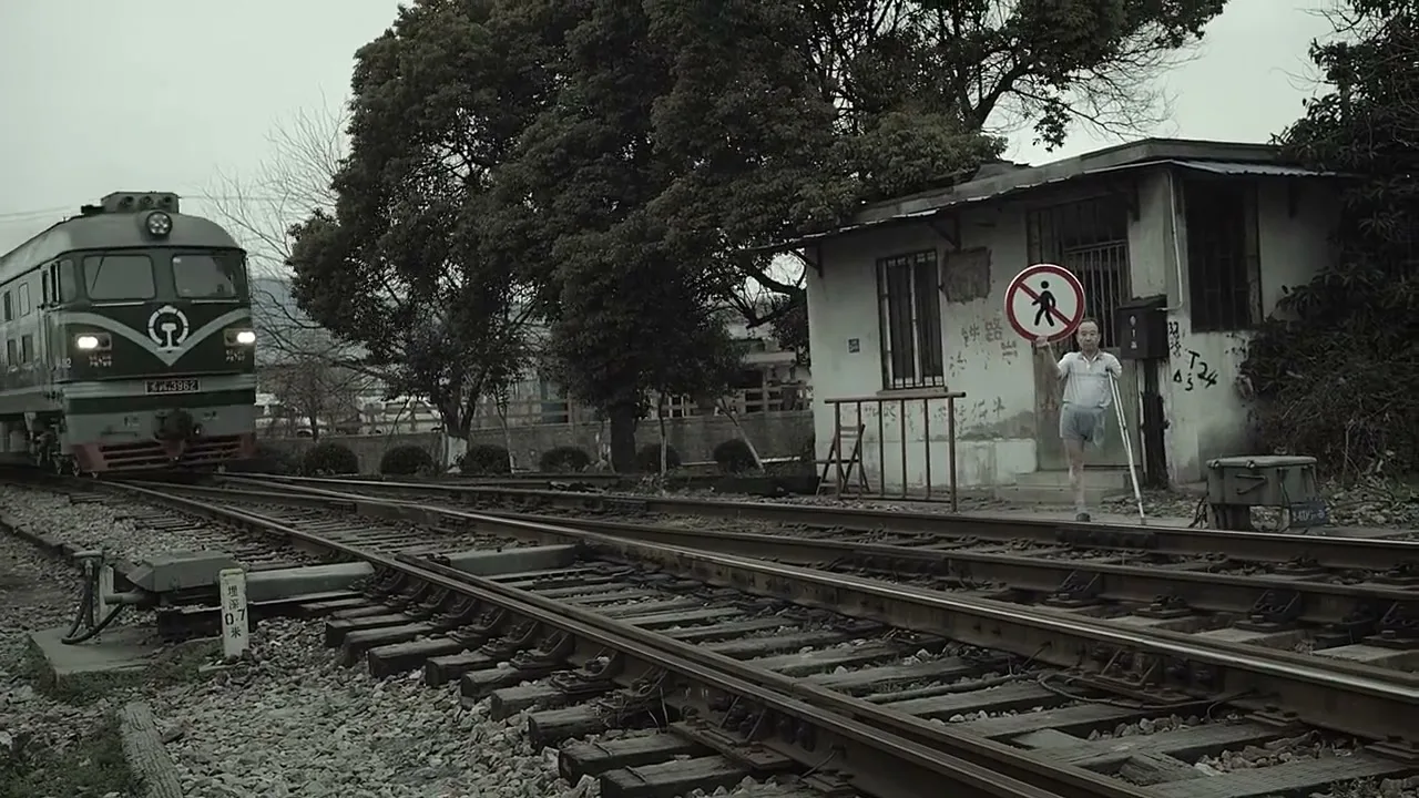 A man on crutches holds a "no pedestrian" sign as a train approaches and passes him on a rural railway track.
