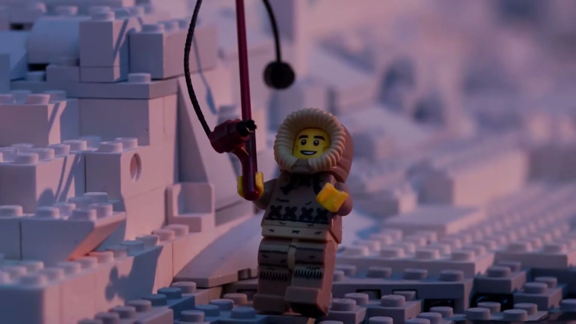 A Lego minifigure dressed in an arctic parka holds a fishing rod, standing on a snowy landscape made of white Lego bricks.