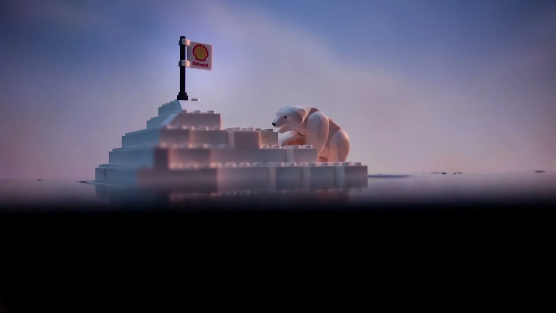 A Lego polar bear sits on a small Lego iceberg with a Shell flag, surrounded by water under a hazy sky.