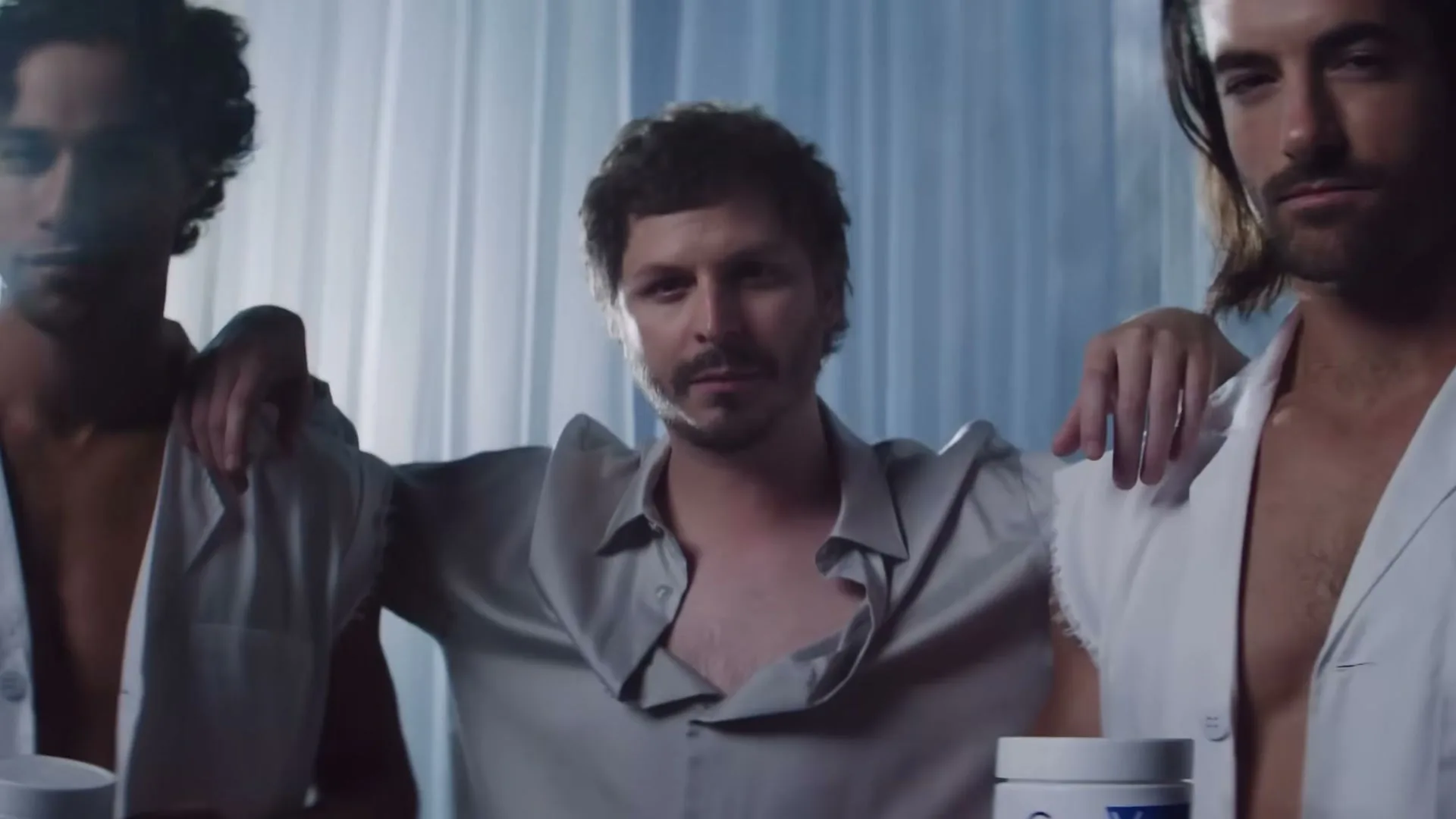 Michael Cera, flanked by two shirtless men in lab coats, holds up a jar of CeraVe cream in a hazy, ethereal setting.