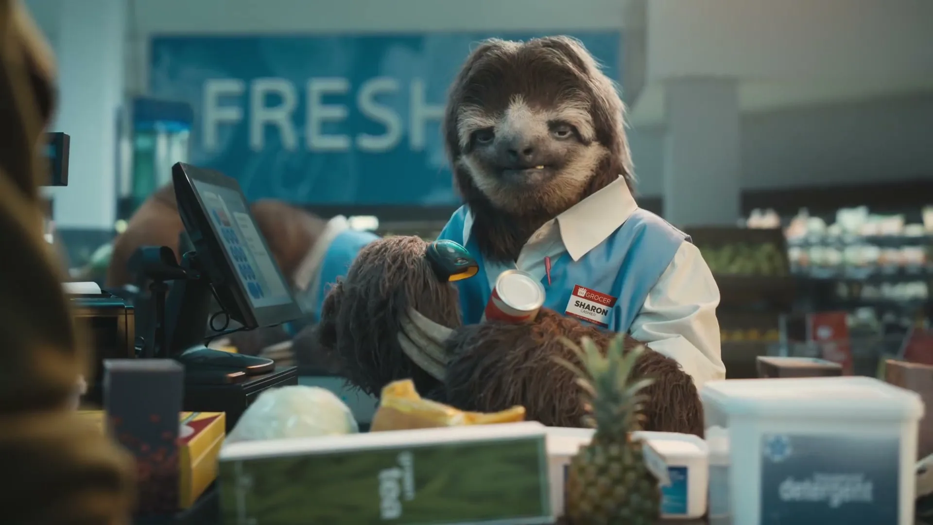 A sloth wearing a grocery store uniform scans a can at a checkout counter, looking at the customer.