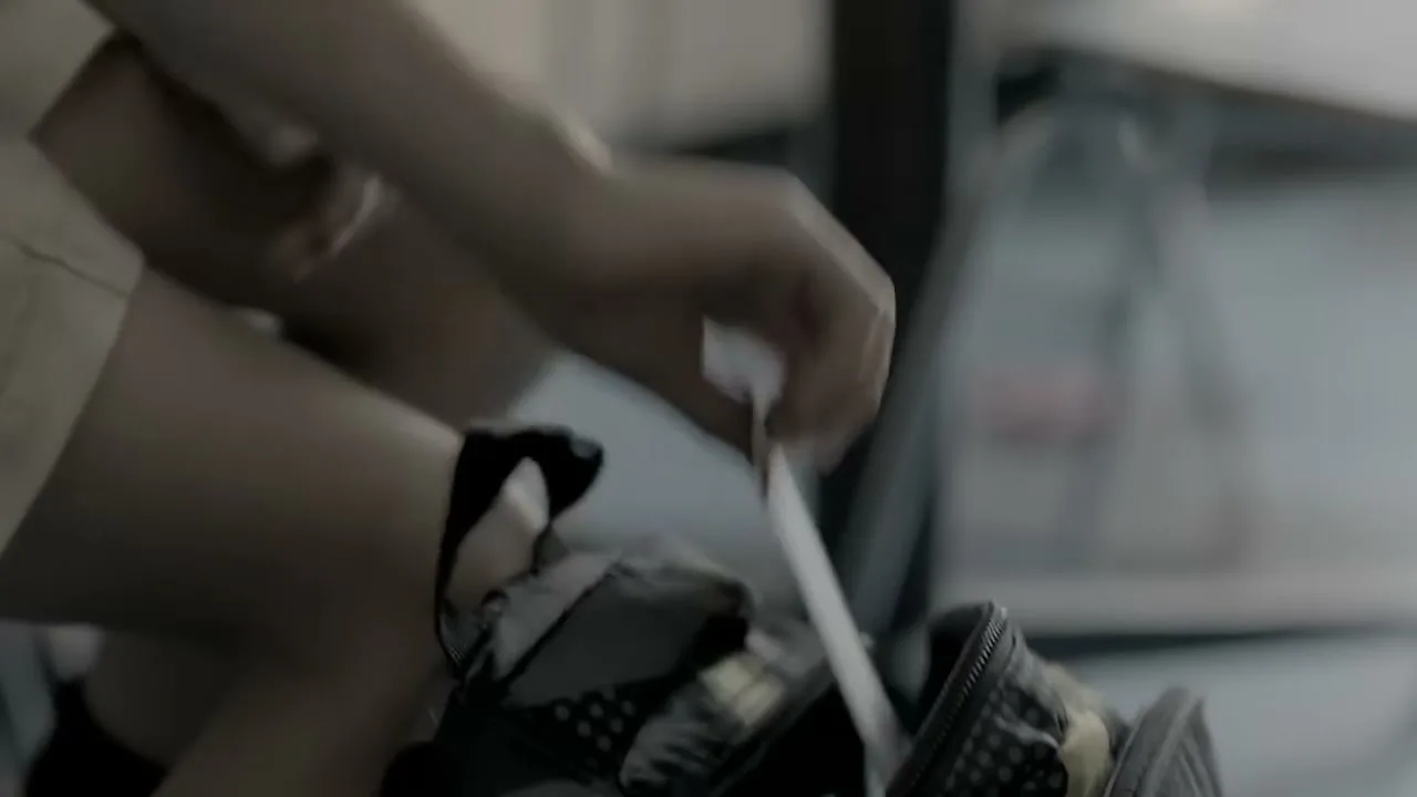 A person in beige shorts reaches into a black bag, pulling out a white object in a blurry, dimly lit interior.