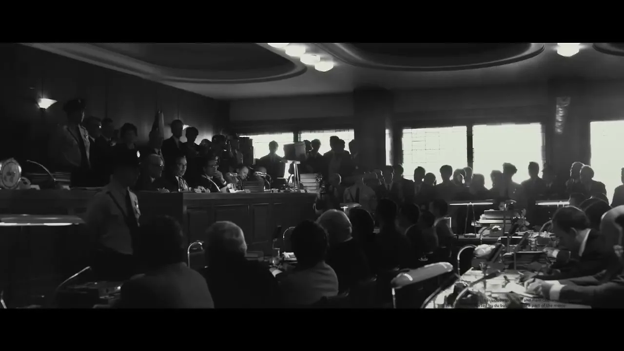 A black and white shot of a large group of men in suits and military uniforms gathered in a formal meeting room, with some seated at tables and others standing.