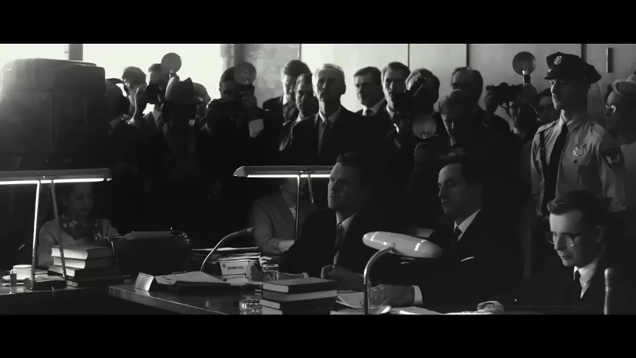 A black and white shot shows a crowded courtroom or press conference with men in suits and a police officer, as reporters take notes and photographers flash bulbs.