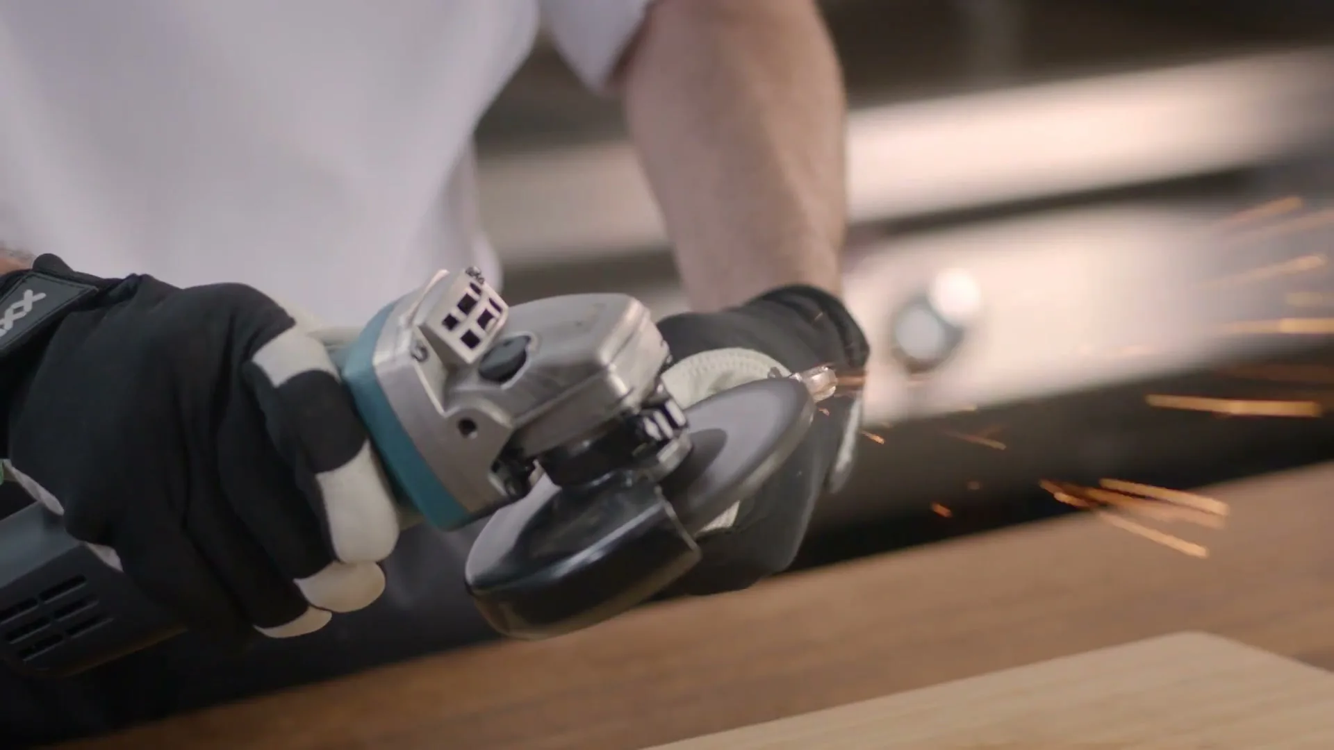 A person wearing black and white gloves uses an angle grinder, creating sparks as they work on a wooden surface in a kitchen.