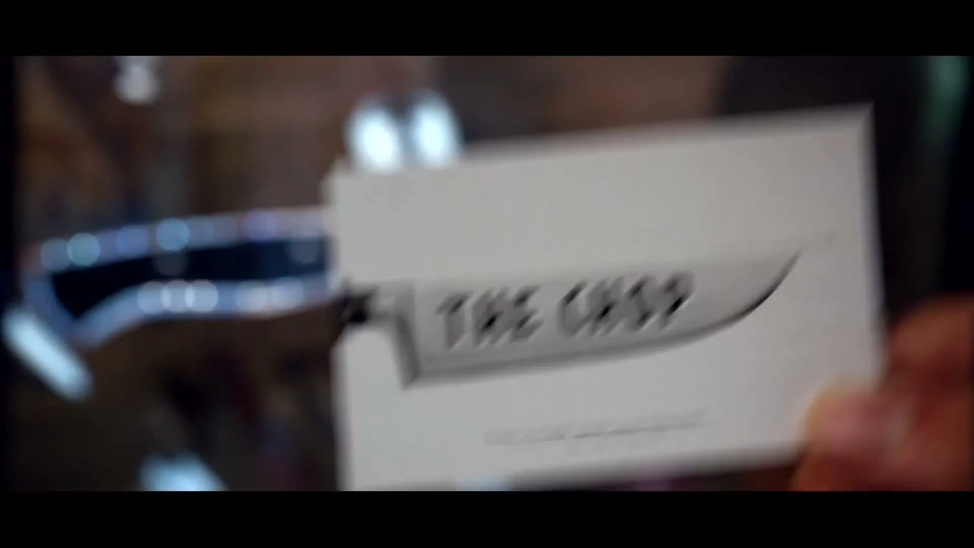 A hand holds up a business card for "The Chop" with a knife logo, then pulls it away to reveal a neon sign for the same shop.