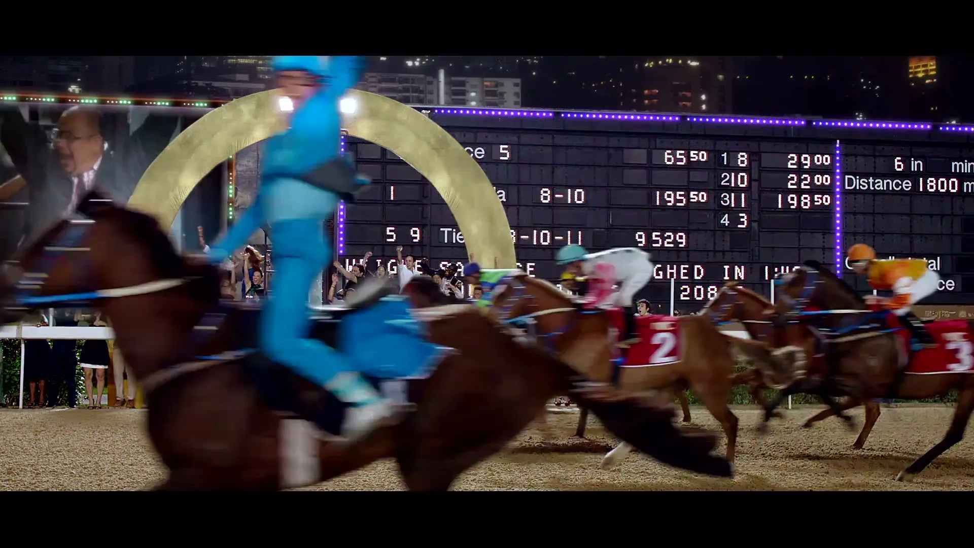 A man in a suit is superimposed over a crowd watching a horse race at night, with a scoreboard in the background.