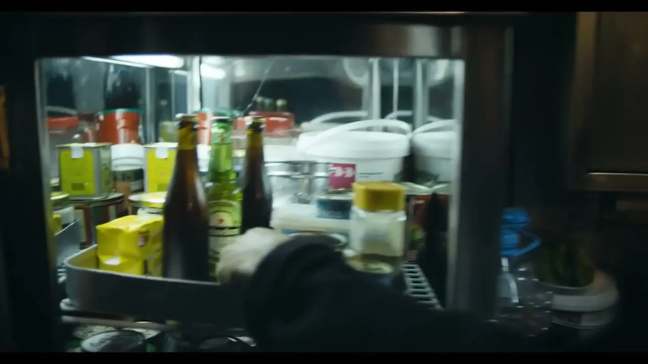 A man in a dark blue jacket opens a small refrigerator on a boat, revealing bottles and cans inside.