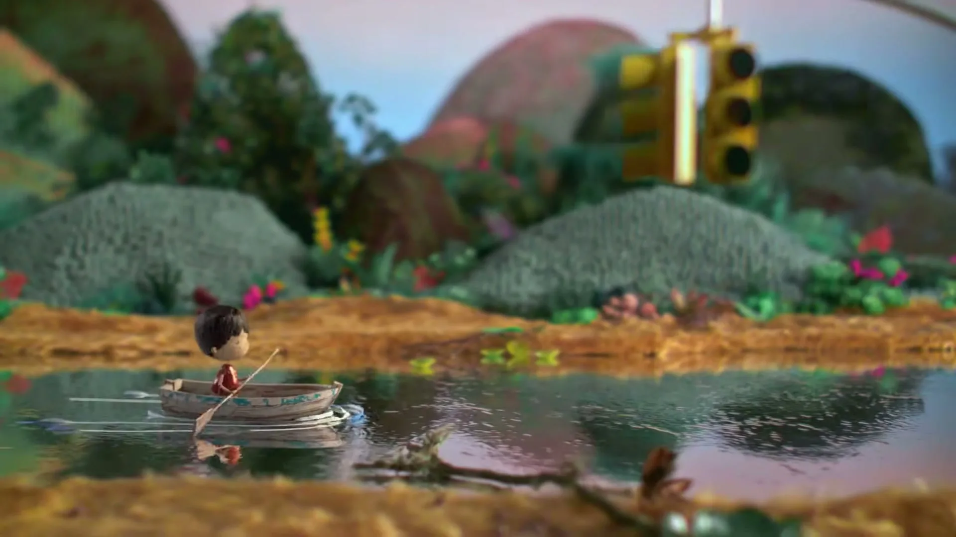 A small, stylized boy in a red shirt rows a tiny boat across a calm body of water, surrounded by a whimsical, textured landscape with hills and a traffic light.
