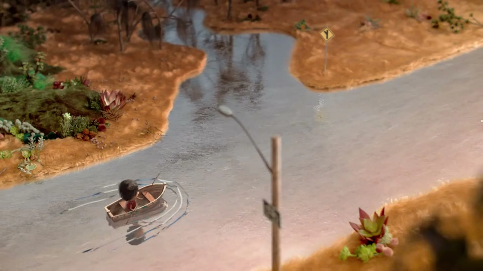 A small, dark-haired child in a brown boat rows down a river, passing a street lamp and a yellow road sign in a miniature, stylized landscape.