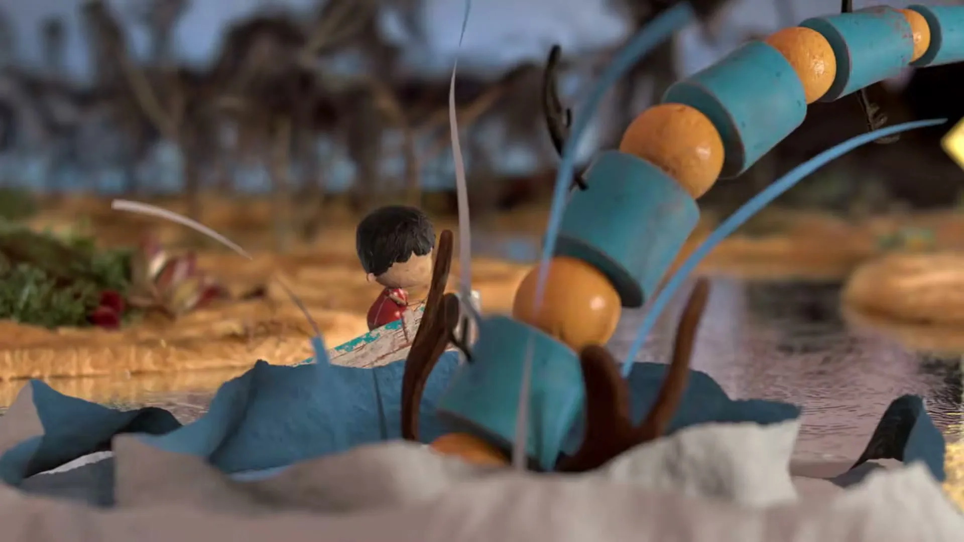 A stop-motion animated boy in a small boat encounters a large, segmented, orange and blue obstacle in a river, with a blurry natural background.