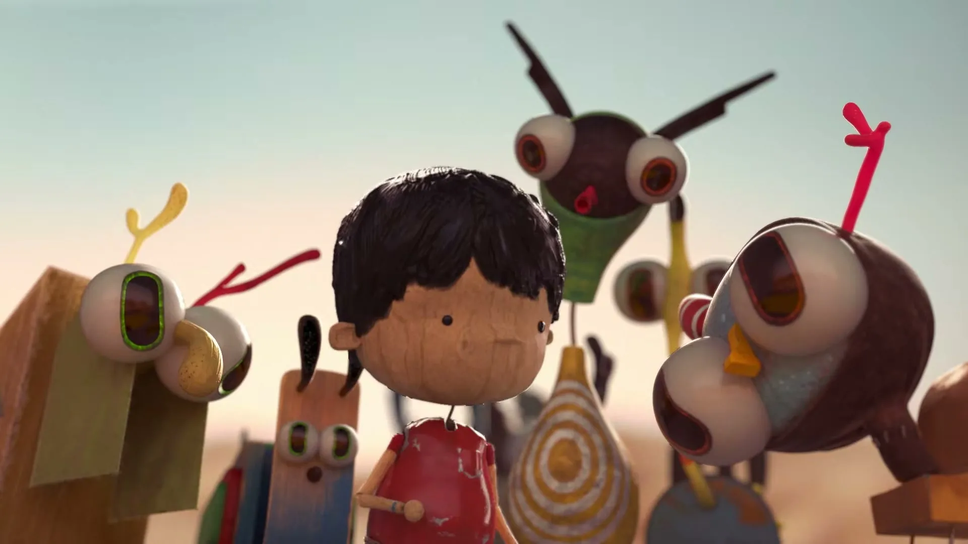 A stop-motion animated boy with dark hair and a red shirt stands among several colorful, abstract creatures with large eyes in a desert-like setting.