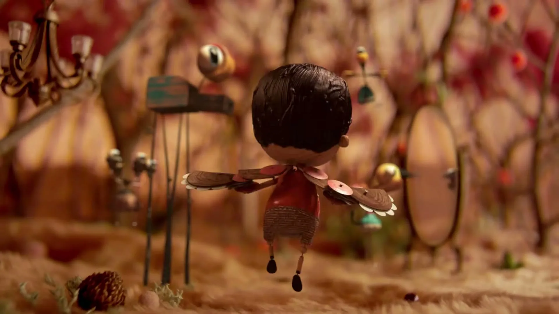 A stop-motion animated boy with dark hair and a red shirt stands with arms outstretched, then floats upwards in a whimsical, fantastical landscape.