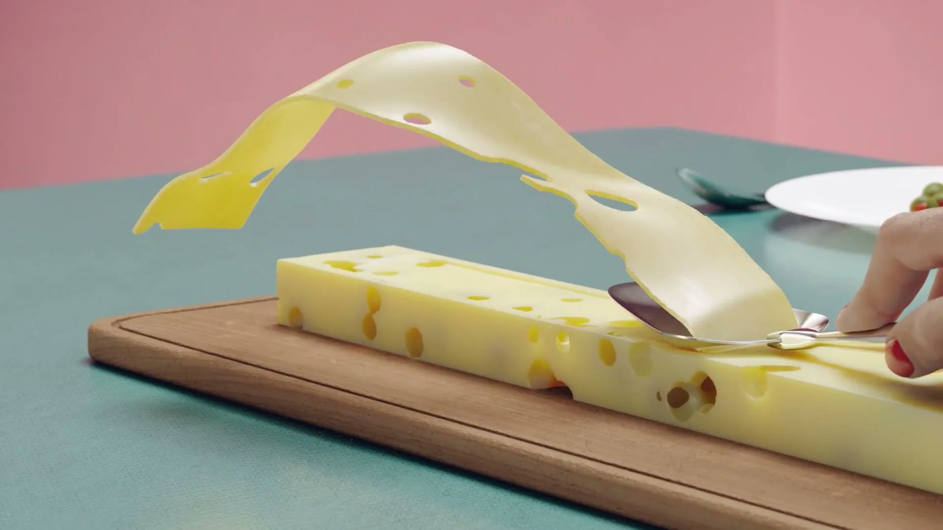 A woman's hand with red nail polish uses a cheese slicer to peel a long, thin slice of Swiss cheese from a block on a wooden cutting board.