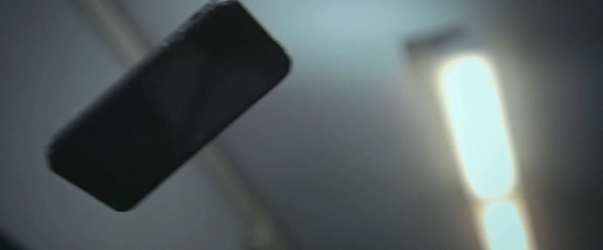 A black smartphone with a rugged case slowly rotates in mid-air against a blurry background with a bright vertical light.