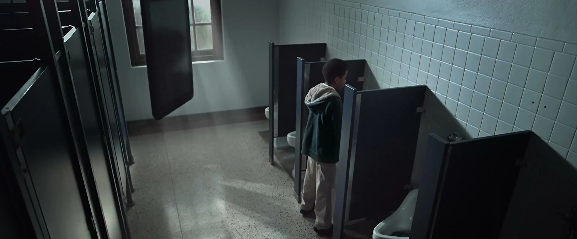 A young boy stands at a urinal in a dimly lit public restroom, while a large smartphone floats ominously nearby.