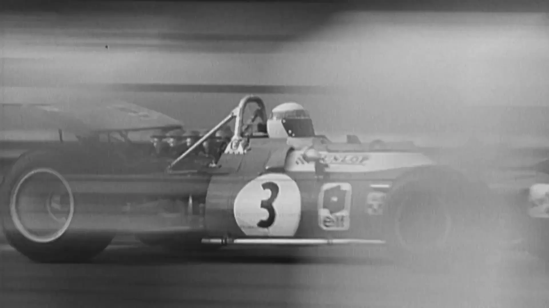 A black and white archival shot shows a race car speeding past a crowd of spectators and a man waving a checkered flag at a finish line.