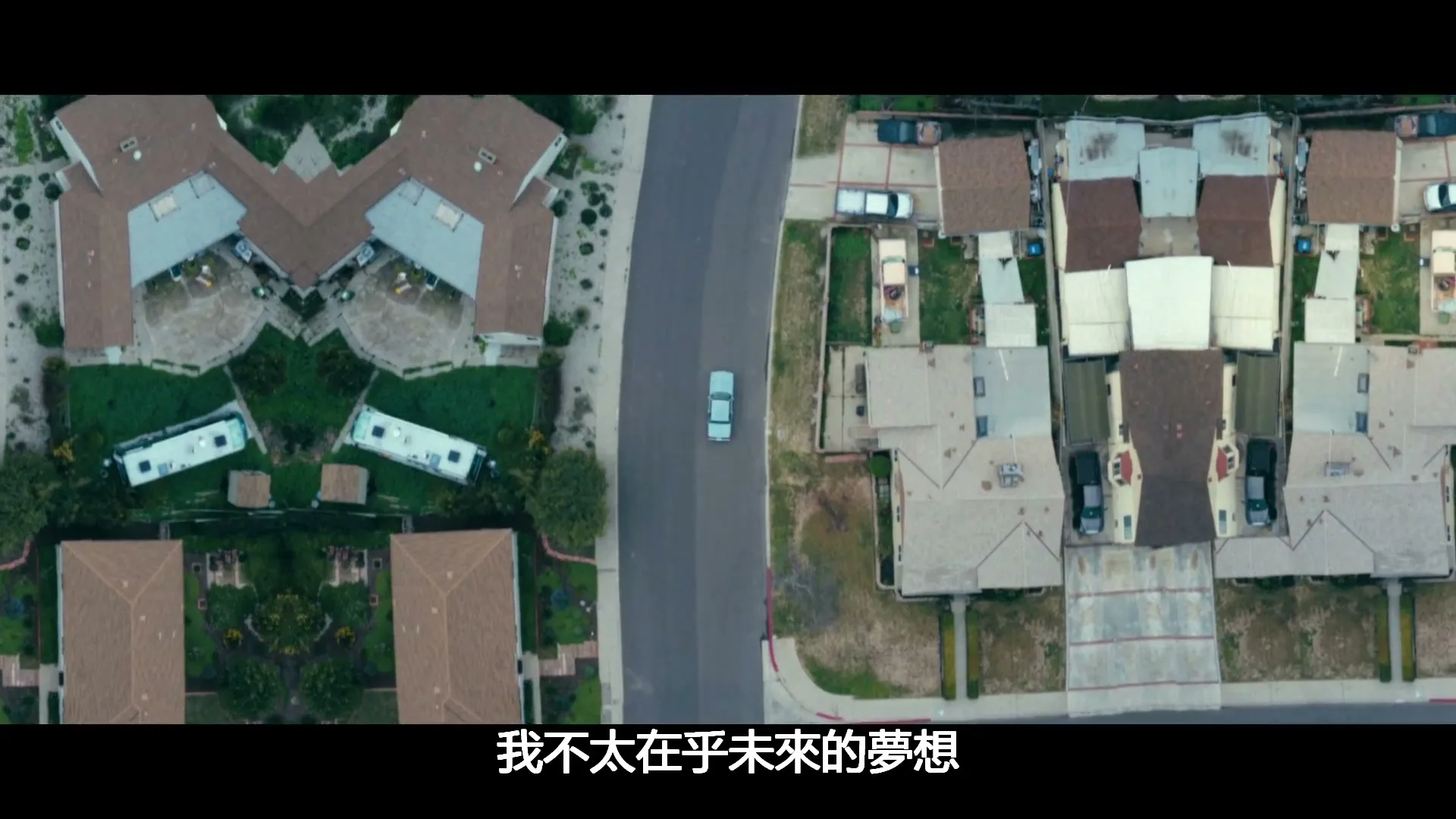 An aerial view of a suburban neighborhood with houses and streets, mirrored on both sides, as a car drives down the middle road.