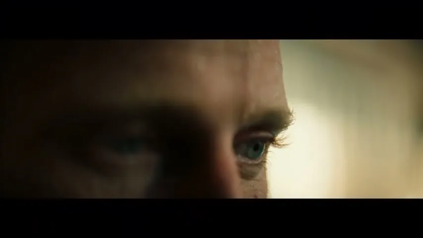 A man with blue eyes and sweat on his brow looks intently to the right, with a blurred background.