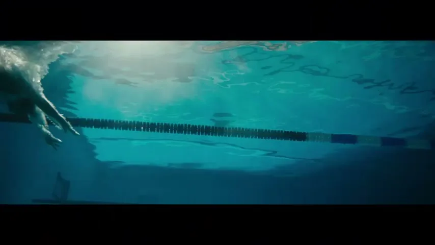 An underwater shot shows a swimmer's arm stroking through the water next to a lane line in a swimming pool.