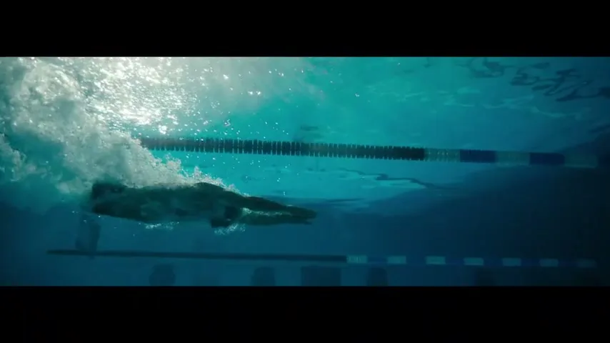 An underwater shot shows a swimmer's body and arm creating bubbles as they swim in a pool.