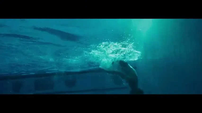 A young male swimmer, seen underwater, pushes off the wall of a swimming pool, creating splashes as he propels himself forward.