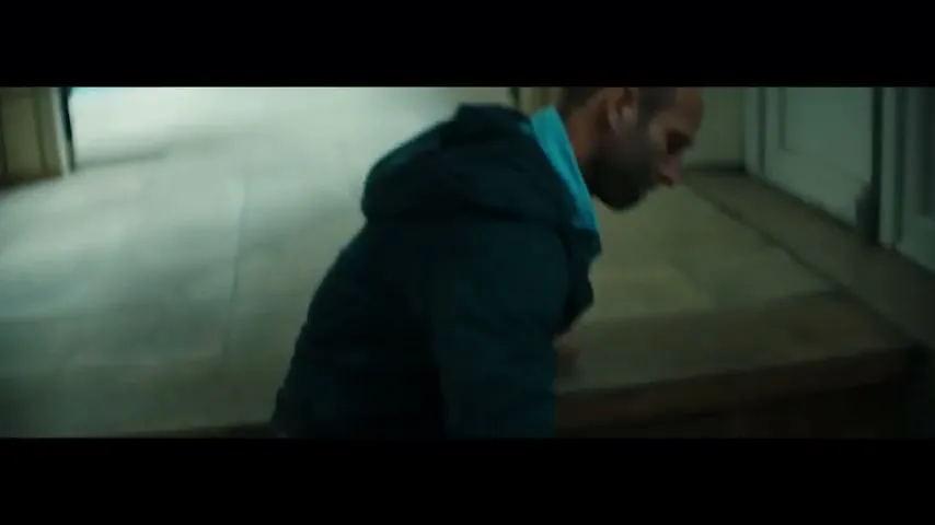 A male swimmer in a dark tracksuit struggles to climb stairs, using his hands and knees, in a dimly lit building.