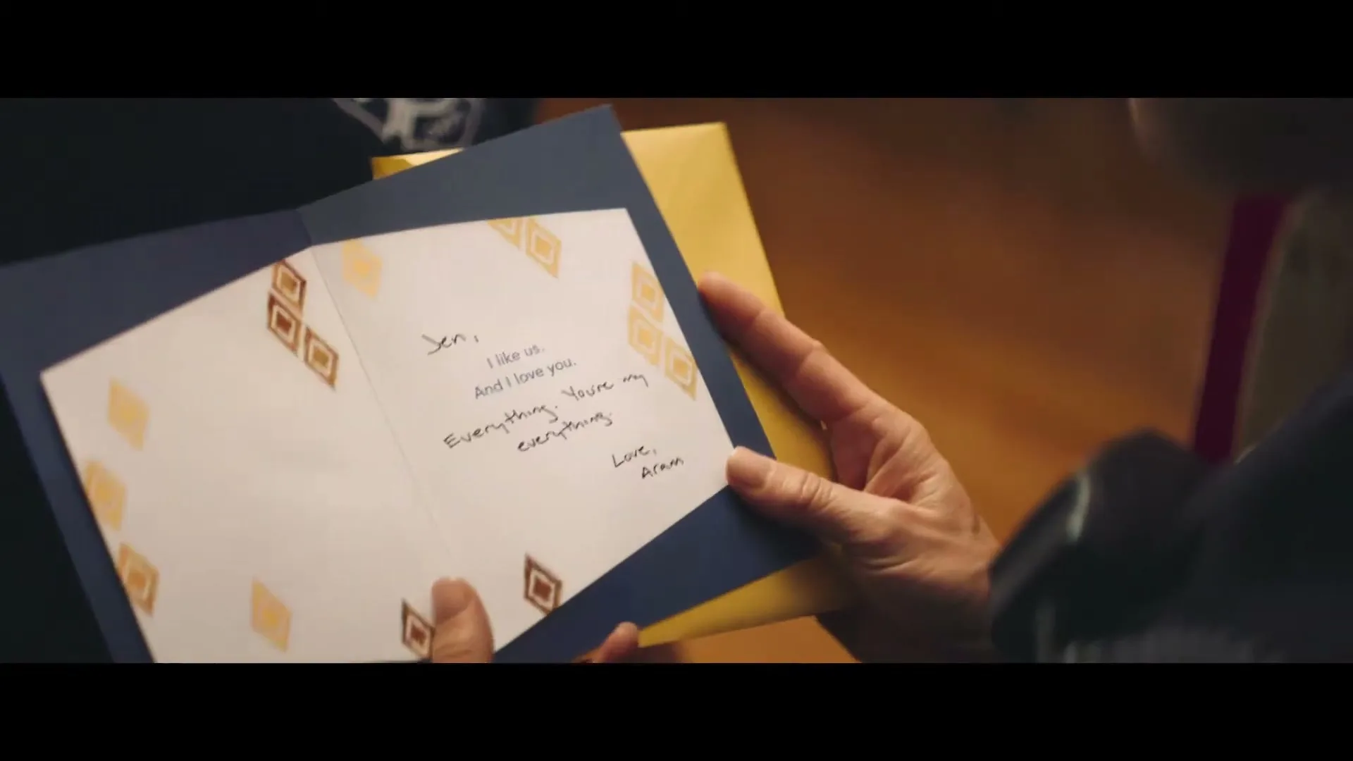 A person's hands hold an open greeting card with a handwritten message, revealing a heartfelt note inside, in a warm, intimate setting.