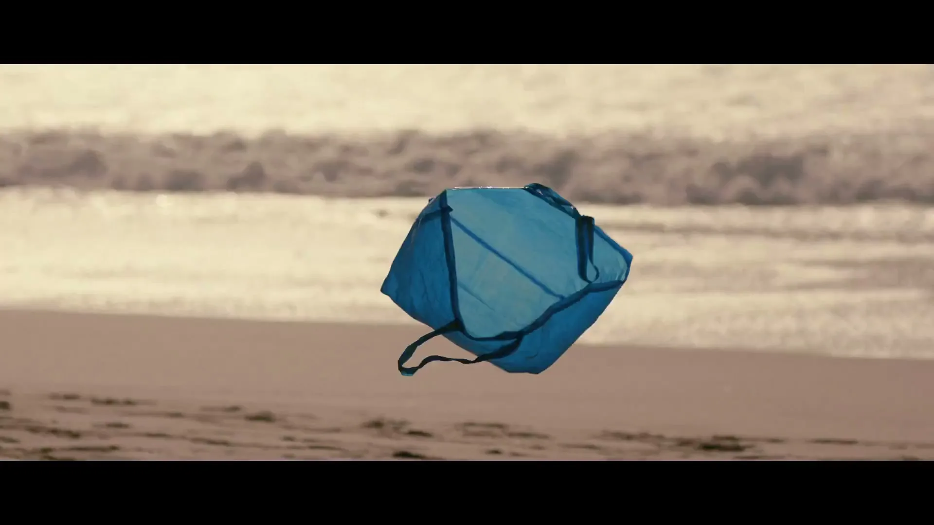 A blue IKEA bag floats above a sandy beach with ocean waves in the background.