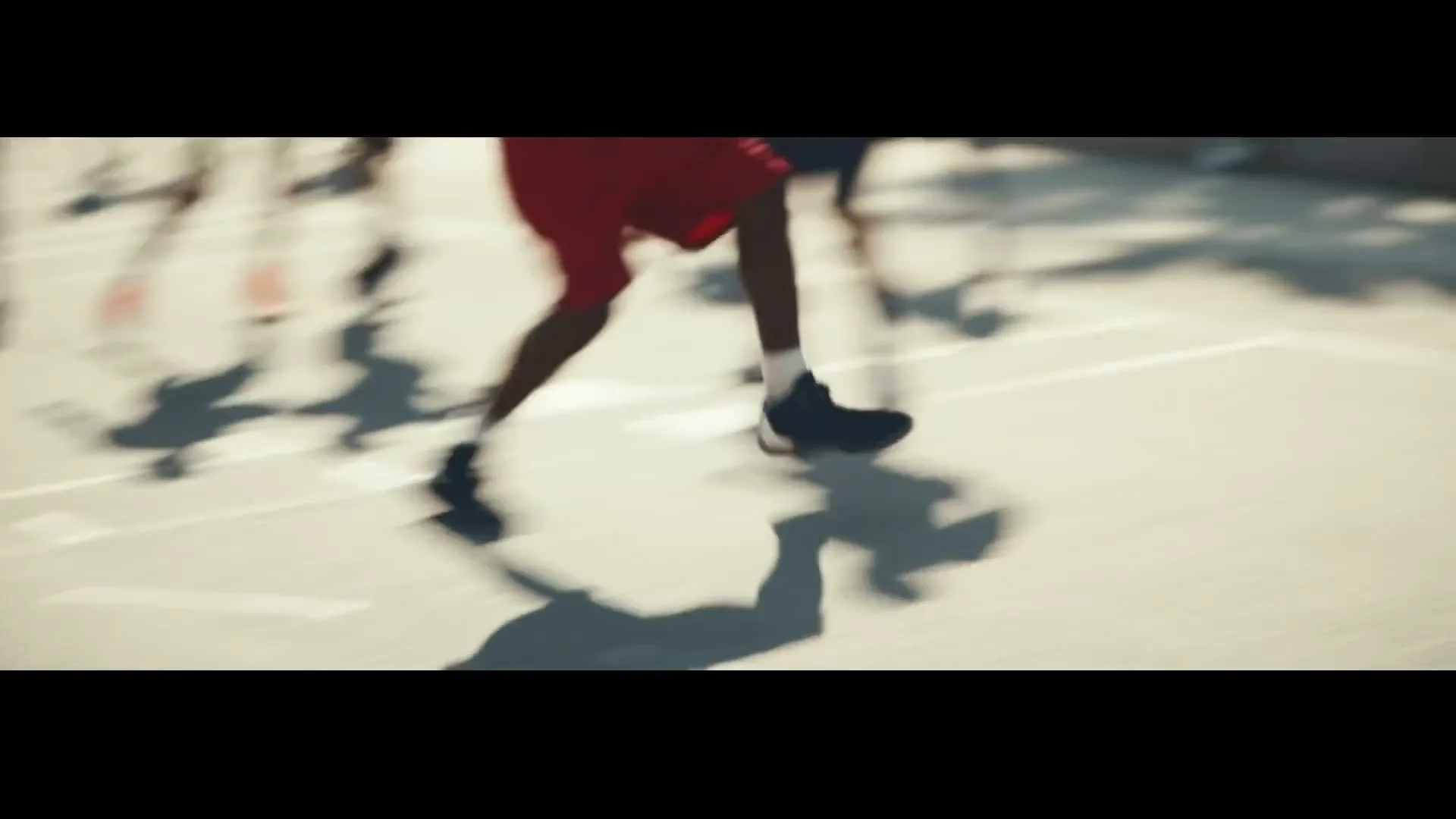 A diverse group of young adults plays basketball on an outdoor court near a beach with palm trees, as one player dunks the ball.