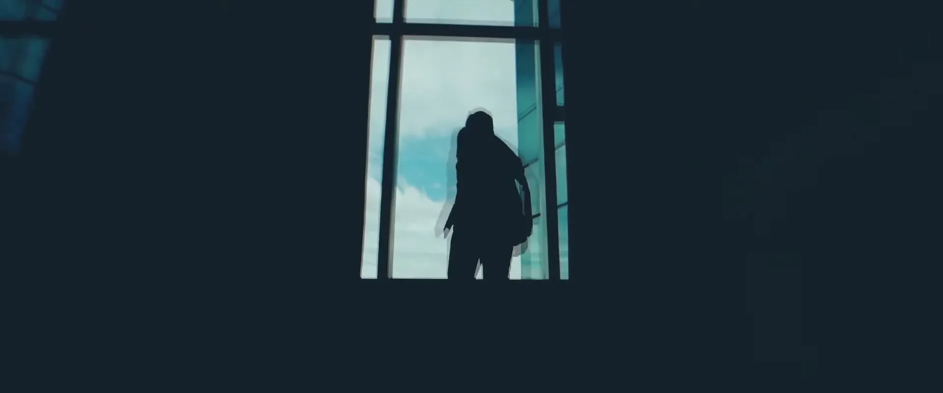 A silhouetted man stands in front of a large window, looking out at the sky, then turns to the side.