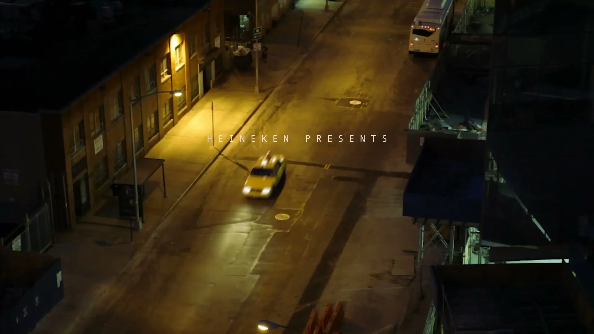 An overhead shot shows a yellow taxi driving down a dark, empty city street at night, illuminated by streetlights.