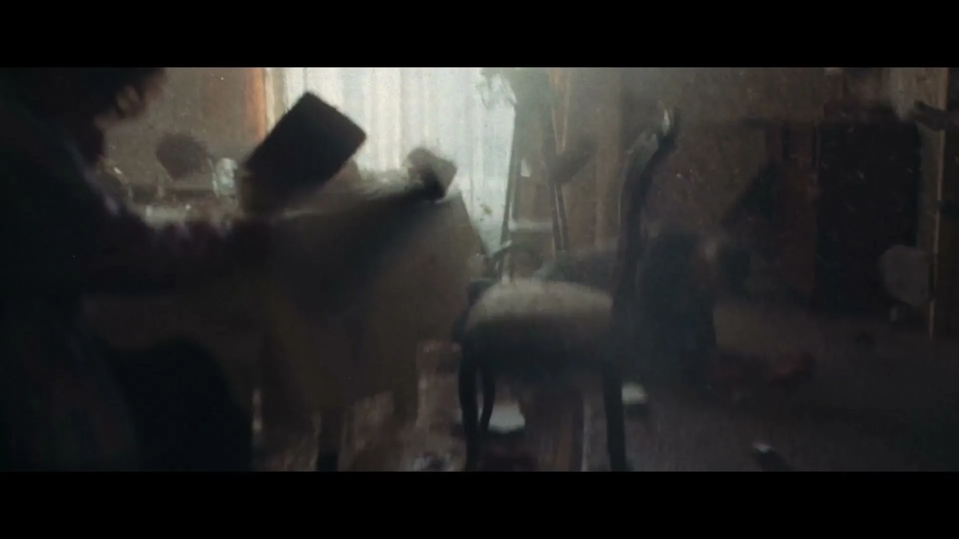 A woman in a purple robe sits at a dining table, holding her head in distress as the room shakes violently, with objects falling and dust filling the air.