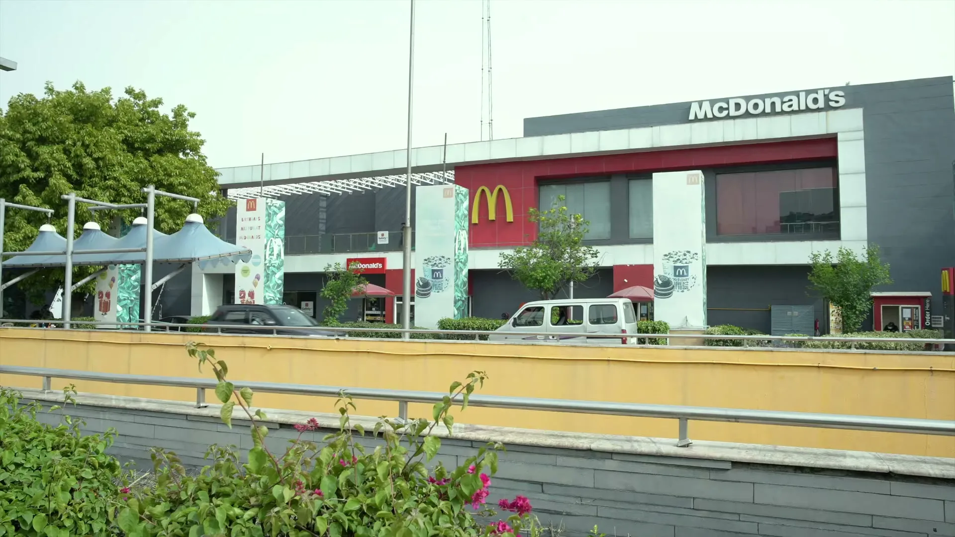 A wide shot of a modern McDonald's restaurant building with cars driving by on a road in front of it during the day.