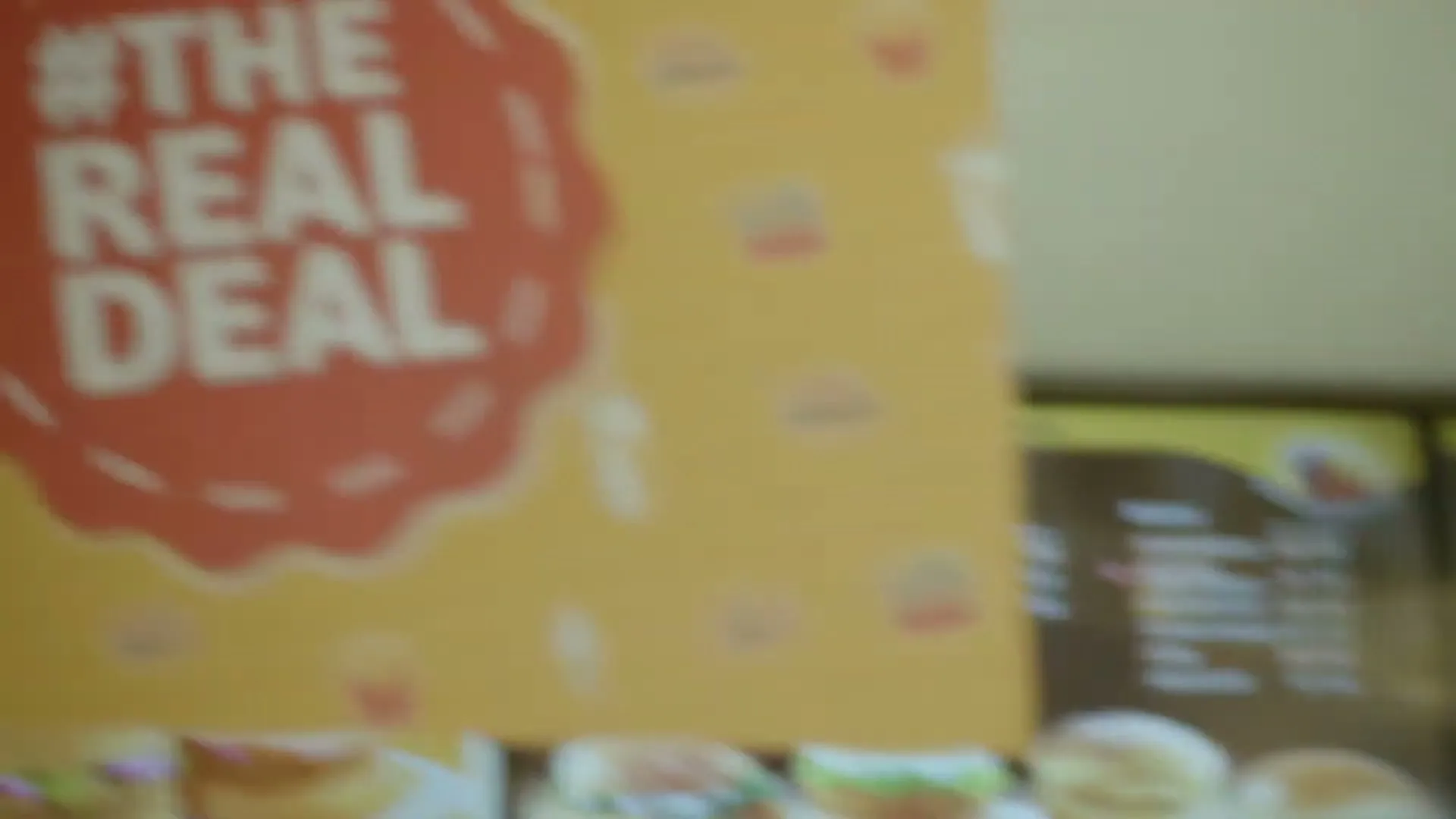 A close-up shot of a McDonald's menu board and a promotional sign with the text "#THE REAL DEAL" in a fast-food restaurant.