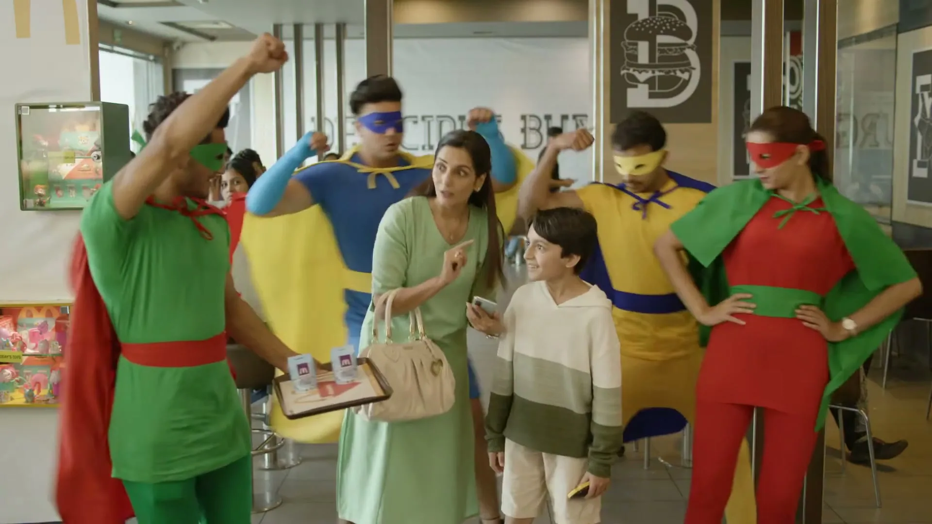 A mother and her son are in a McDonald's restaurant when a group of people dressed as superheroes appear around them, surprising the mother.