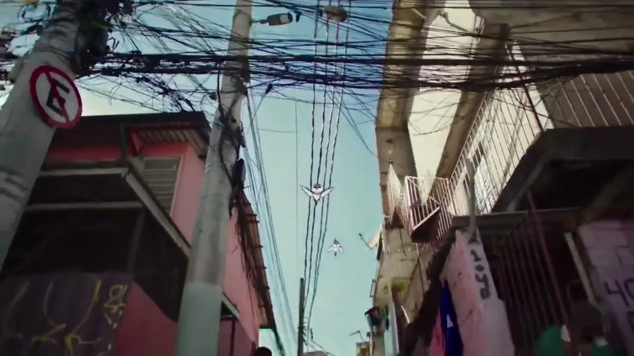 A low-angle shot captures a chaotic tangle of power lines against a bright sky, with buildings on either side, as a person walks by.