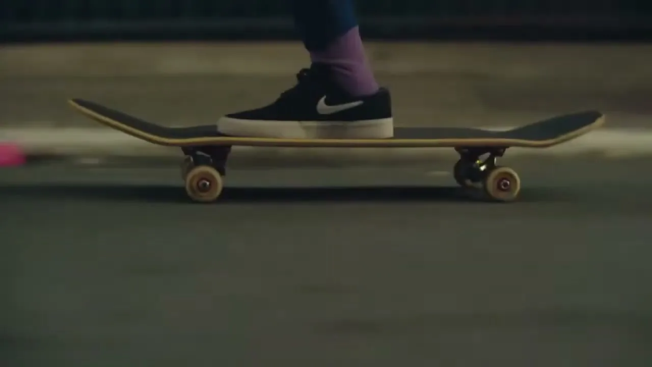 A person's feet, wearing black Nike sneakers and purple socks, are seen on a skateboard as they ride along a street at night.