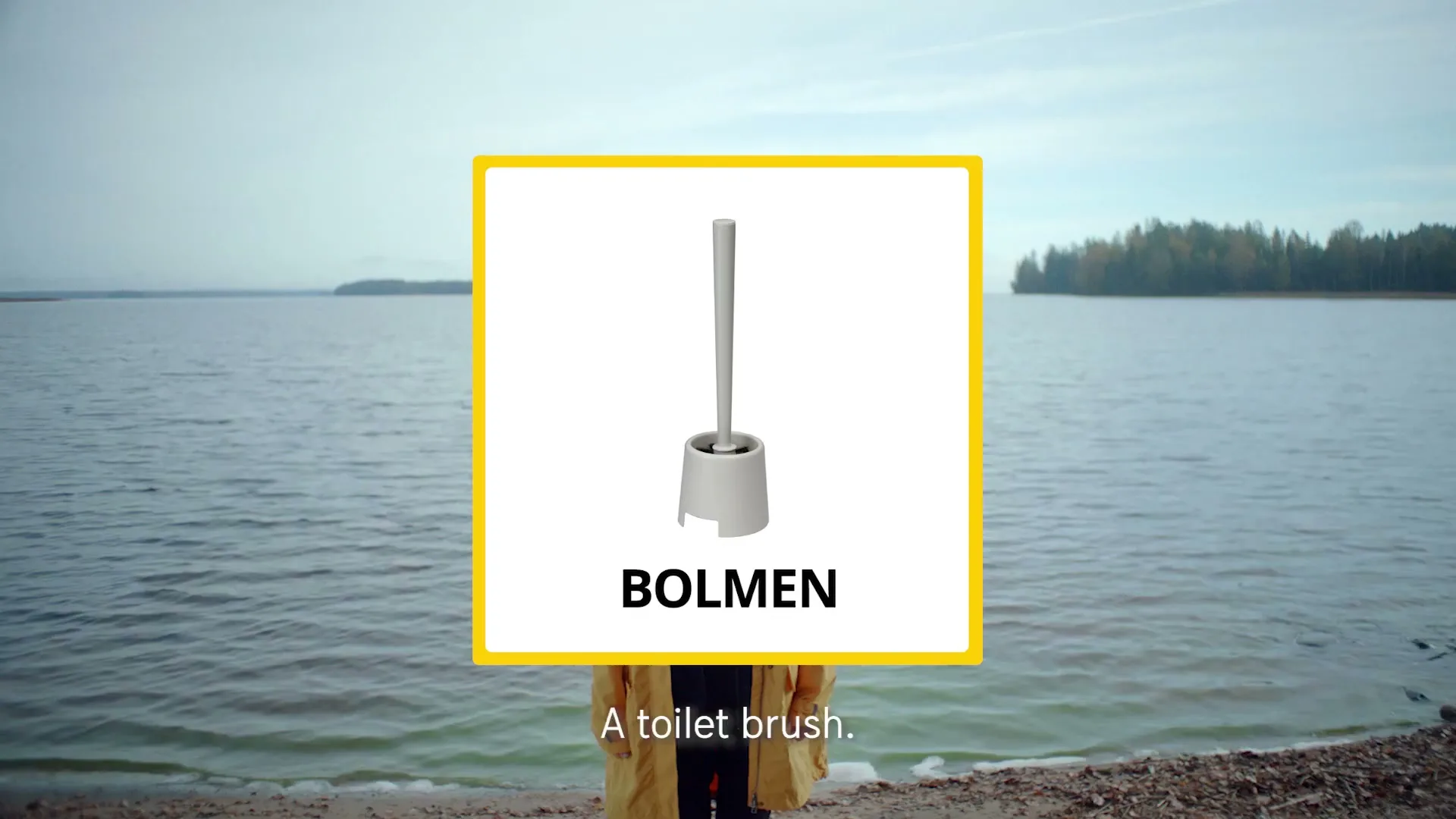 A person stands on a beach with a lake and forest in the background, while a graphic of a toilet brush with the word "BOLMEN" covers their face.