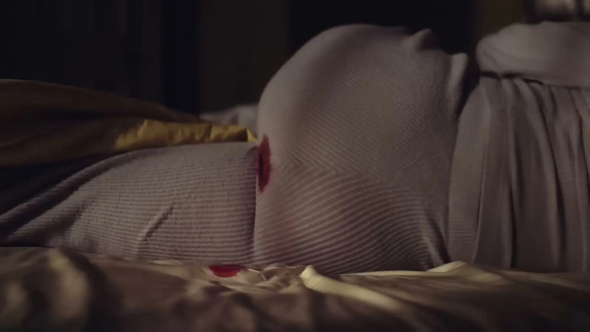 A woman in bed, covered by a duvet, has a period stain on her nightgown and the bedsheet.