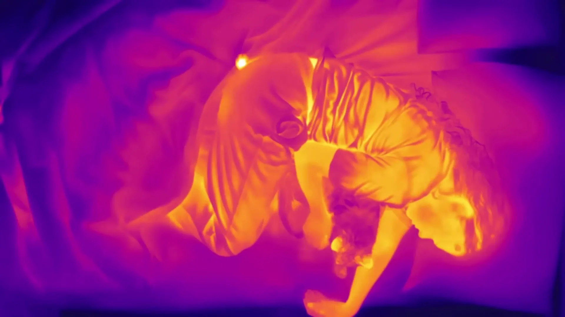 A woman in thermal imaging colors, curled up in bed, struggling to sleep due to period discomfort.