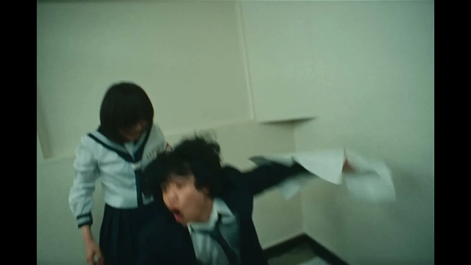 A male student lies on the floor covered in papers, then a female student helps him up, and finally, a female dancer performs in a classroom.