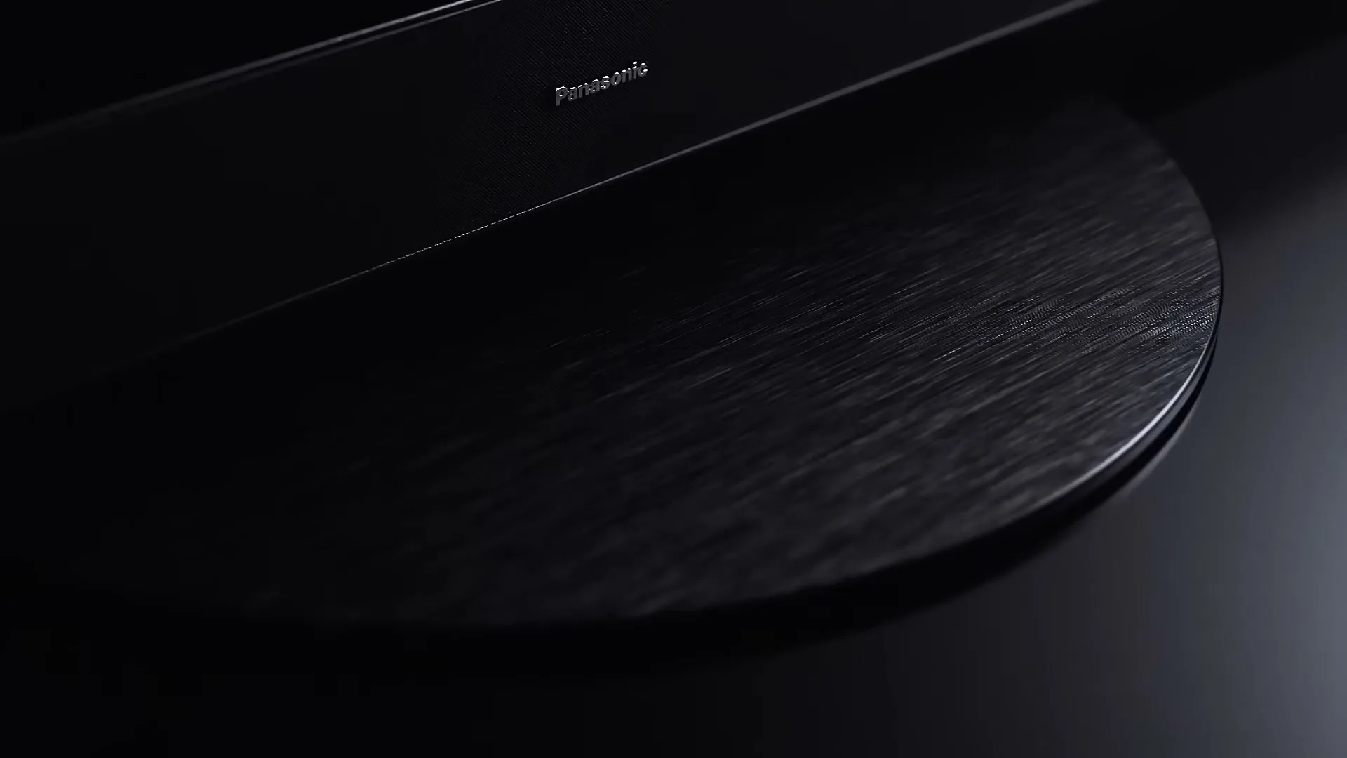 A close-up shot of a black Panasonic soundbar and a circular brushed metal base, slowly panning right in a dark setting.