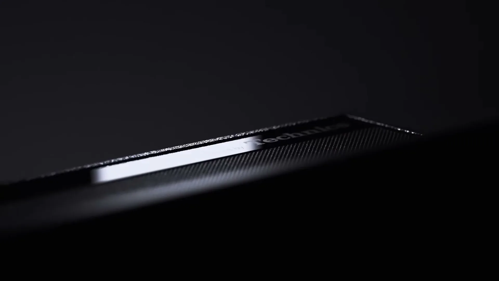 A close-up shot of a black speaker with the text "Tuned by Technics" visible, slowly revealing itself from darkness.