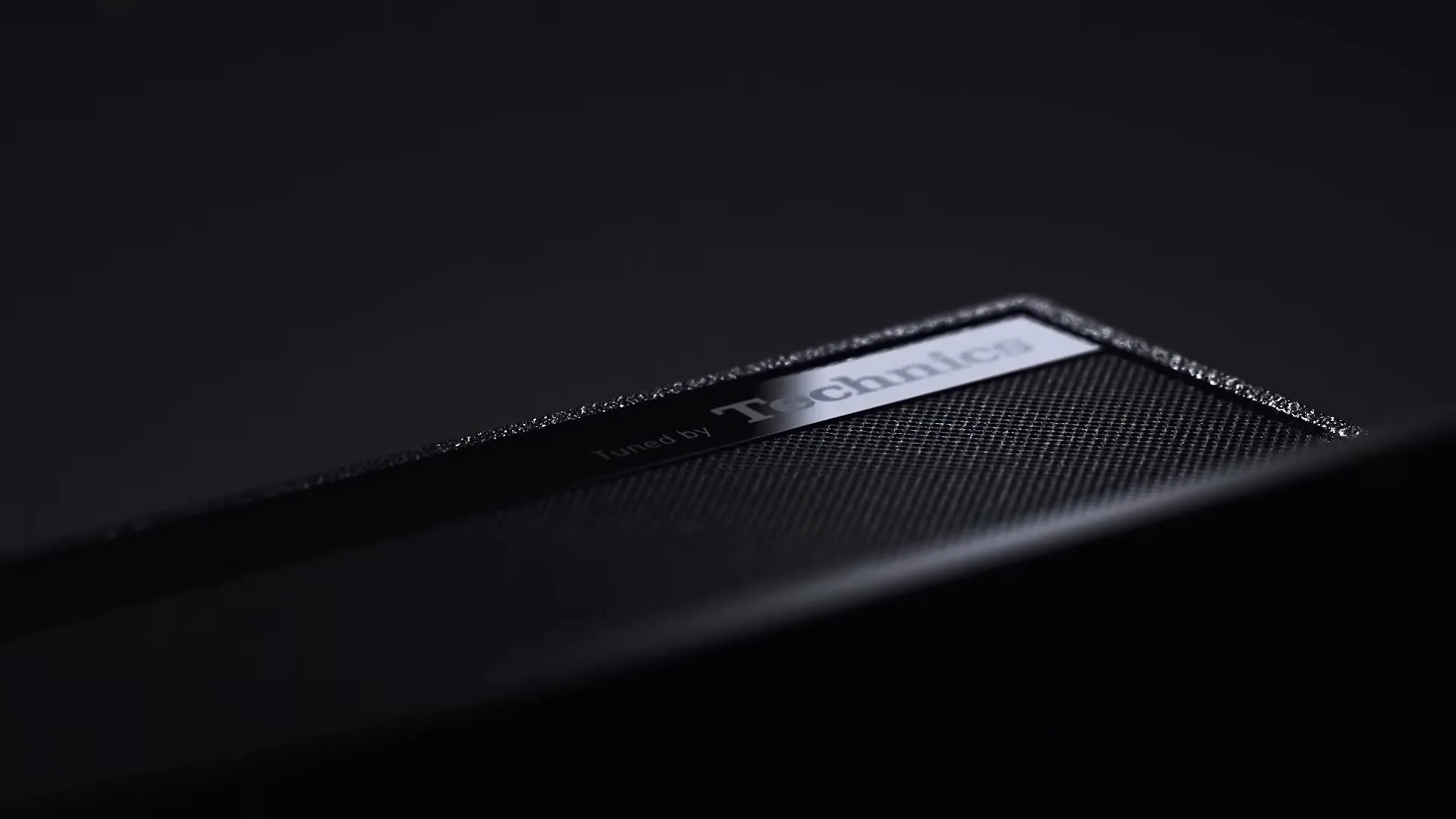 A close-up shot of a black Technics speaker with a reflective surface, showcasing its brand name in a dark, minimalist setting.