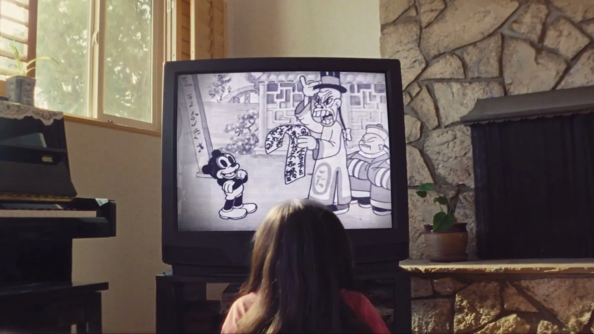 A young girl with long dark hair sits on the floor, watching a black and white cartoon on an old television in a cozy living room.