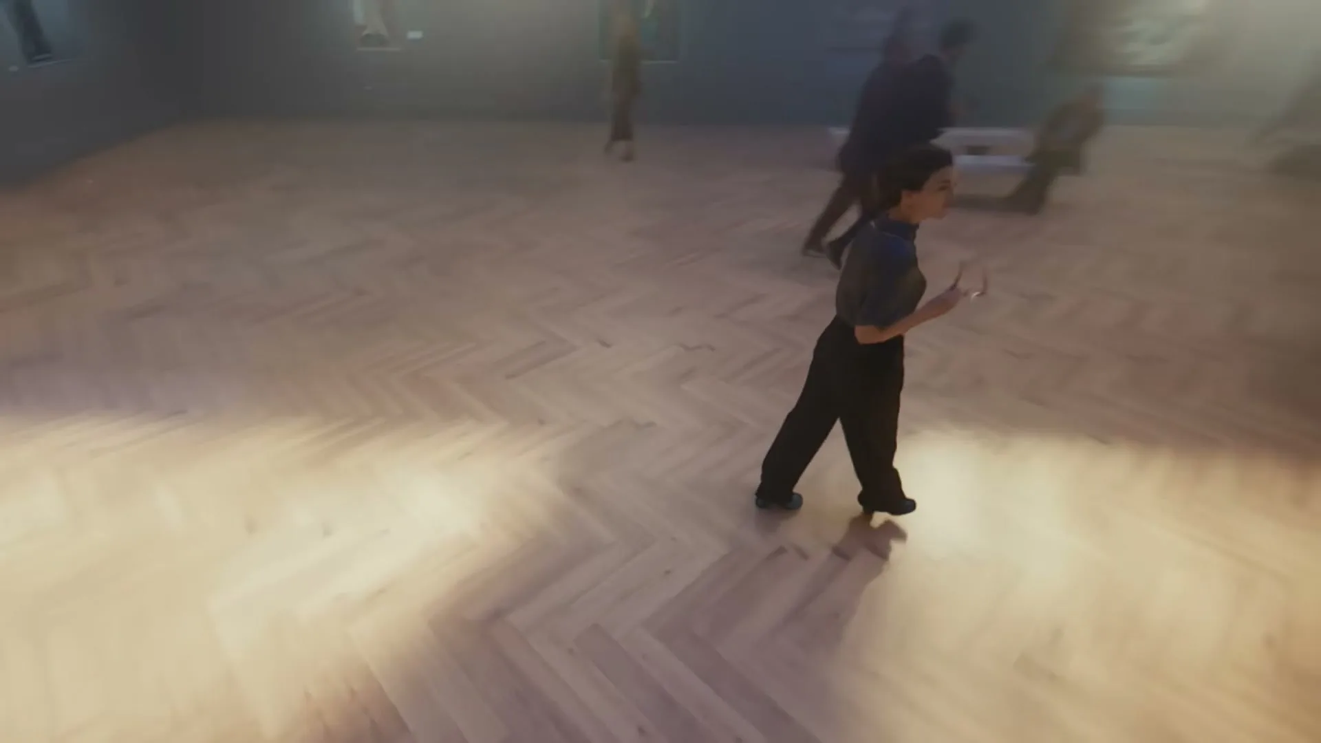 A drone shot descends from the exterior of a museum, through a window, and into the interior, revealing a young man sketching amidst other museum-goers.