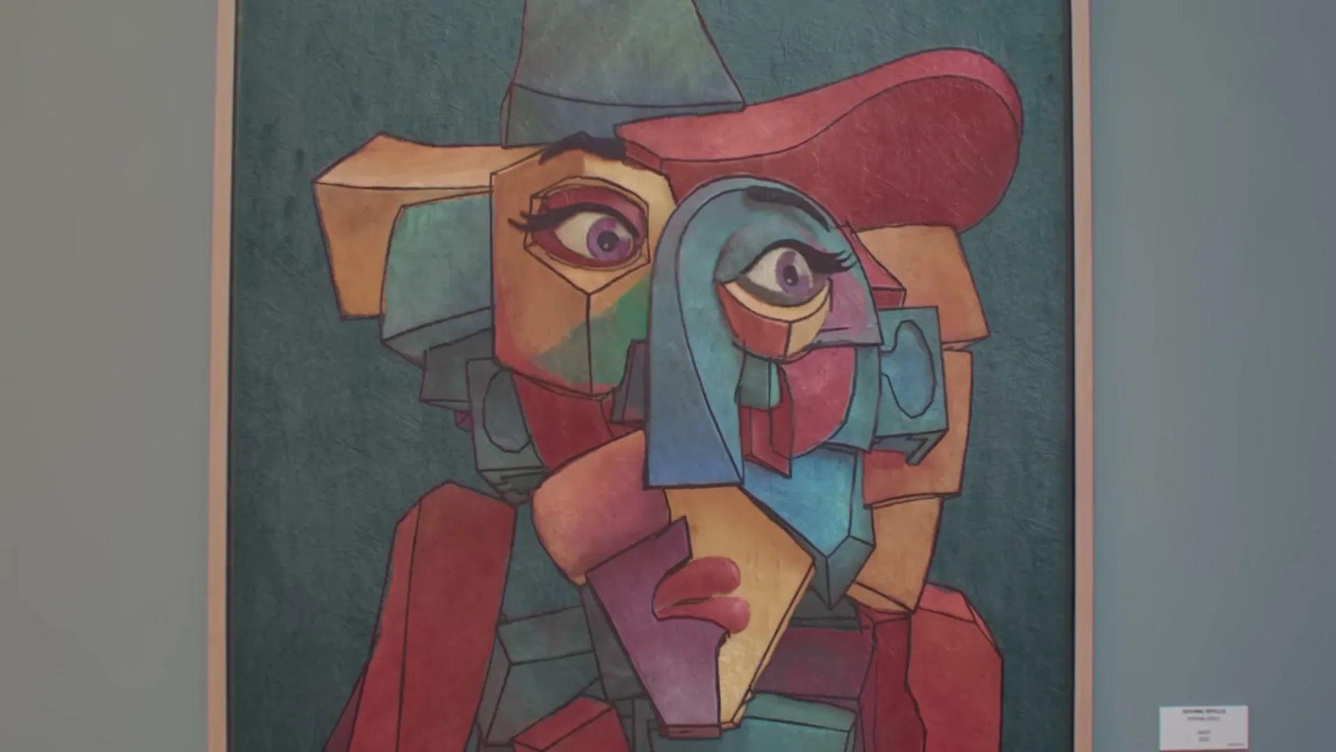 A colorful, cubist-style painting of two faces, one male and one female, is displayed on a wall in an art gallery.